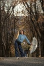 Girl with long hair poses in fall park. Woman is dressed in sweater and pants and holds transparent umbrella in hands