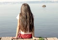 A girl sits on the edge of a pier near the water and looks into the distance Royalty Free Stock Photo