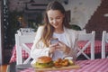 Girl with a long hair sitting in a restaurant. Girl food blogger takes a picture on the phone from social networks