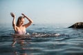 Girl with long hair, in a striped swimsuit, bathes in the ocean, laughs, plays and splashes
