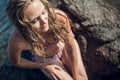 Girl with long hair, in a striped swimsuit, sits on the rocks, on the ocean, on a bright sunny day