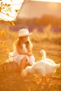 A girl with long hair and a white hat feeds the ducks on a summer sunset evening.