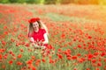 A girl in a red dress weaves wreaths of poppy flowers in a poppy field.