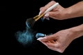 A girl with a long manicure applies blue powder to a brush. Small particles of powder are all around. close-up