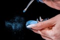 A girl with a long manicure applies blue powder to a brush. Small particles of powder are all around. close-up