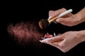 A girl with a long manicure applies red powder to a brush. Small particles of powder are all around. close-up