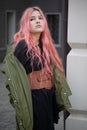 A girl with long pink hair stands and looks to the side, she is wearing a Basco belt