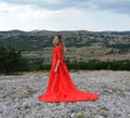 A girl in a long scarlet dress in a forest in the mountains