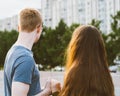 Girl with long thick dark hair holding hands redhead boy in blue t-shirt on bridge, teen love at evening. Boy looks tenderly at