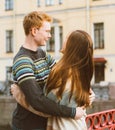Girl with long thick dark hear embracing redhead boy in the blue t-shirt on a bridge, young couple. Concept of teenage love and Royalty Free Stock Photo