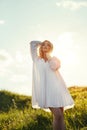 Girl in a long white dress dancing in the field. Blonde woman in the sun in a light dress. Girl resting and dreaming, perfect