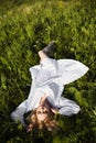 Girl in a long white dress lies on the grass in a field. Blonde woman in the sun in a light dress. Girl resting and dreaming, Royalty Free Stock Photo