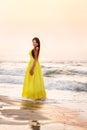 A girl in a long yellow dress walks by the sea in the early morning