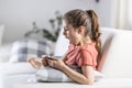 Girl looking into her phone yawns from being tired or bored as she sits at home on a sofa Royalty Free Stock Photo