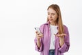 Girl looks confused at smartphone, receive strange message on phone, complaining, looking puzzled, standing over white