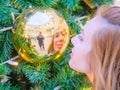 A girl looks at her distorted reflection in a golden ball hanging on a Christmas tree Royalty Free Stock Photo