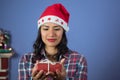 Girl looks at a little Christmas present that holds with her hands wearing santa hat and lumberjack shirt