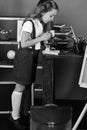 Girl looks into microscope standing by books and bag. Schoolgirl with busy face near bookshelf with school items Royalty Free Stock Photo