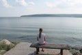 Girl looks at the sea sitting on a bench on the beach