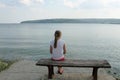 Girl looks at the sea sitting on a bench on the beach