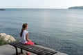 Girl looks at the sea sitting on a bench on the beach