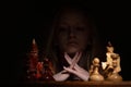 The girl looks thoughtfully at the chessboard against a dark background. old chess. business concept