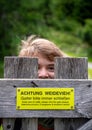 Girl Looks Through Wooden Fence With Yellow Sign With Text `Keep Care Of Cattle, Please Shut The Gates Always!`