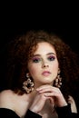 A girl with lush curly red hair. Close face with bright make-up and massive earrings.Purple shadows.Bare shoulders