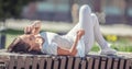Girl lying on a city bench calling on her mobile phone, holding facemask in her right hand