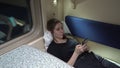 Girl is lying in a compartment car near the window with a phone in her hand and surfing messengers