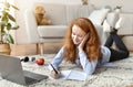 Girl lying on floor carpet, using laptop, writing in notebook Royalty Free Stock Photo