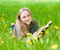 Girl lying on grass with dandelions reading a book and looking at camera Royalty Free Stock Photo