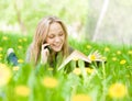 Girl lying on grass with dandelions reading a book and talking Royalty Free Stock Photo