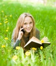 Girl lying on grass with dandelions reading a book and talking Royalty Free Stock Photo