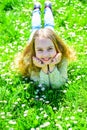 Girl lying on grass at grassplot, green background. Child enjoy spring sunny weather while lying at meadow. Heyday