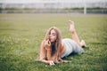 Girl is lying on grass in gray knitted dress, looking with playful look, her back leg is raised up Royalty Free Stock Photo