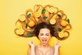 Girl lying with orange fruits in long hair screams in despair, young shocked woman with citrus slices and leaves, emotion splash