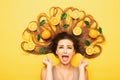 Girl lying with orange fruits in long hair screams in despair, young shocked woman with citrus slices and leaves, emotion splash