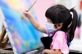 Girl made water painting art in class. Children wear white masks to prevent the spread of virus. Child wear black apron.
