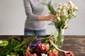 Girl make bouquet over gray background, putting flowers in vase. Royalty Free Stock Photo