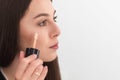 Girl, make-up artist, with long dark hair in a business suit, applies a concealer on the face on a white background Royalty Free Stock Photo