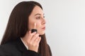 Girl, make-up artist, with long dark hair in a business suit, applies a concealer on the face on a white background Royalty Free Stock Photo