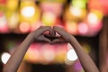 Girl makes heart-shaped hand sign on blurred background of lights to symbolize friendship and loving-kindness towards her lover