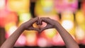 Girl makes heart-shaped hand sign on blurred background of lights to symbolize friendship and loving-kindness towards her lover