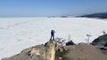 A girl makes a video of a beautiful winter landscape on her phone, standing on a rock near the cliff of Cape Burkhan
