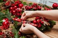 Girl making Christmas door wreath using natural fir branches, red colourful berries, wooden toys, cones and cinnamon sticks. Royalty Free Stock Photo