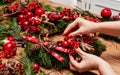 Girl making Christmas door wreath using natural fir branches, red colourful berries, wooden toys, cones and cinnamon sticks Royalty Free Stock Photo