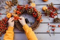 Girl making floral autumn door wreath using colorful rosehip berries, rowan, dry flowers and pumpkin