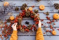 Girl making floral autumn door wreath using colorful rosehip berries, rowan, dry flowers and pumpkins Royalty Free Stock Photo