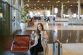 Girl making video call by tablet in airport hall and sitting near valise, showing thumbs up. Royalty Free Stock Photo